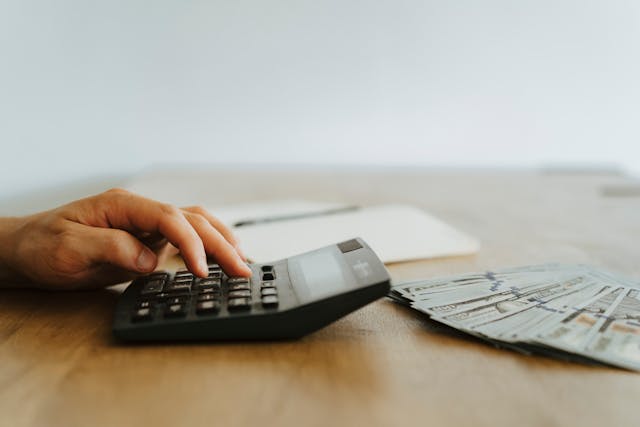 person using a calculator with cash next to them on a desk